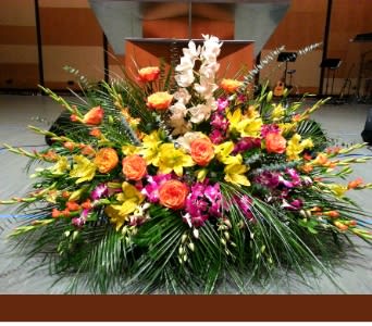Large stage arrangement with yellow lilies, orange roses, and pink orchids in a fan-shaped design