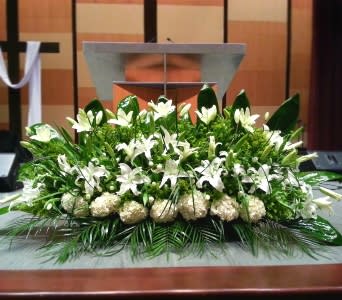 Low, elongated white lily and hydrangea arrangement on a stage in front of a podium