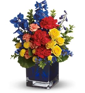 Colorful bouquet of red, yellow, blue, and peach flowers in a square vase