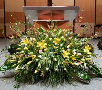 Large low yellow and white lily arrangement with abundant greenery in front of a podium