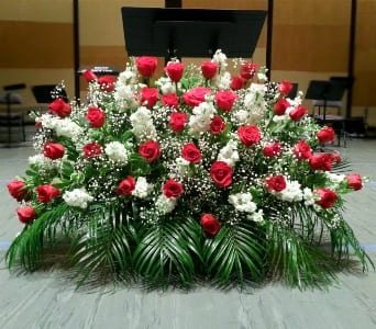 Large fan-shaped arrangement of red roses and white flowers with palm fronds on a stage.