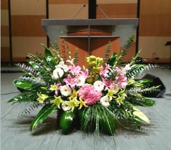 Large stage arrangement of pink lilies, white flowers, and lush greenery in front of a podium