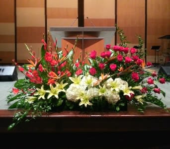 Large altar floral arrangement with pink roses, white hydrangeas, lilies, and tropical blooms.