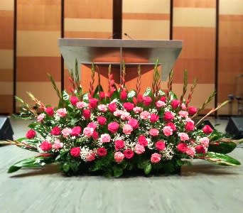 Large pink and white floral stage arrangement with roses and carnations in front of a podium.