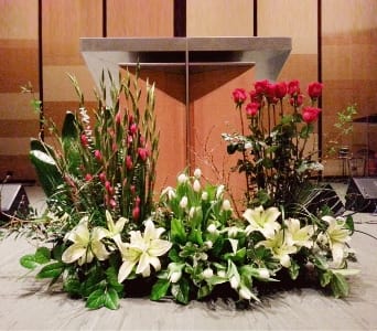 Large altar floral arrangement with white lilies, tulips, and red roses in front of a podium