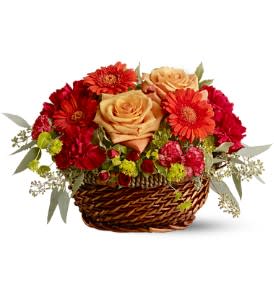 Low basket arrangement with peach roses, orange gerberas, red carnations, and green accent blooms