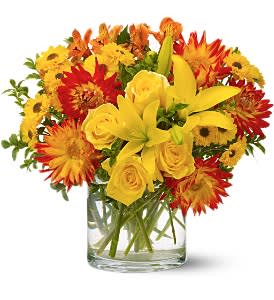 Yellow roses and lilies in a clear glass vase with red and orange daisies