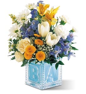 Mixed bouquet in a blue glass cube vase with white, yellow, and blue flowers