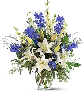 White lilies and blue flowers in a clear glass vase