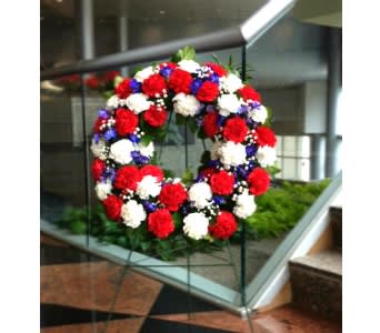 Patriotic wreath of red, white, and blue flowers displayed on a metal easel stand.