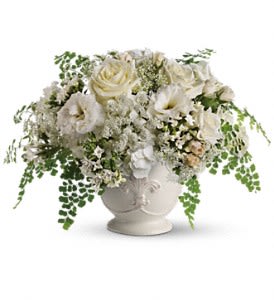 Low white rose and lisianthus arrangement in a white ceramic urn with cascading fern accents
