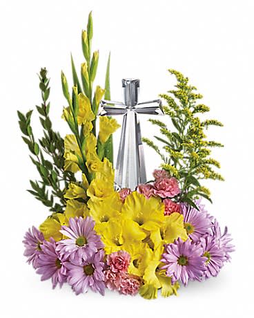 Religious floral arrangement with yellow and lavender blooms surrounding a clear crystal cross.