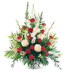 Tall red and white floral sympathy arrangement in a white vase with prominent greenery.