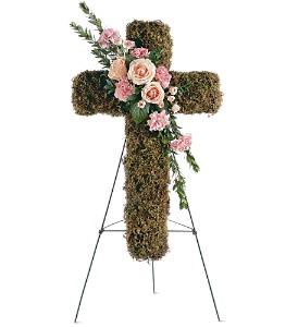 Standing moss-covered cross with pink and peach flowers on a metal easel.