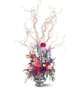 Tall mixed flower arrangement with curly branches in a silver pedestal vase