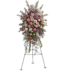 Tall standing spray of pink roses, carnations, and purple flowers on a metal easel