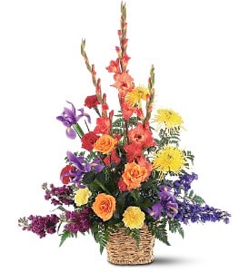 Tall mixed basket arrangement with orange gladiolus, roses, yellow mums, and purple flowers