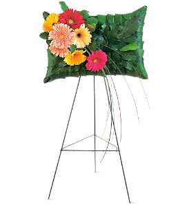 Pillow-shaped green leaf display with bright gerbera daisies on a tall metal easel.