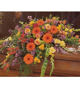 Bright mixed floral casket spray in orange, yellow, and purple on a wooden casket