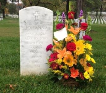 Colorful basket of yellow, orange, and red flowers placed beside a white cemetery headstone