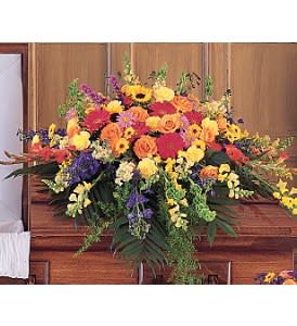 Bright mixed funeral casket spray of yellow, orange, and red flowers on a wooden casket