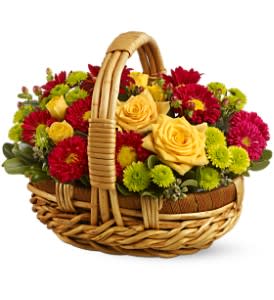 Low basket arrangement of yellow roses with red, pink, and green mums.