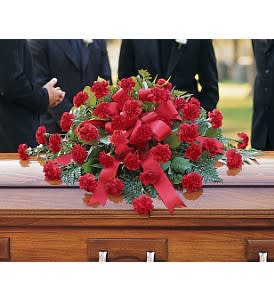 Red carnation casket spray with red ribbon on a wooden casket at a funeral service