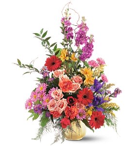 Tall mixed arrangement of pink roses, red gerbera daisies, carnations, and assorted bright flowers in a gold vase