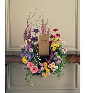 Colorful mixed flower wreath with central memorial card displayed on a wooden surface