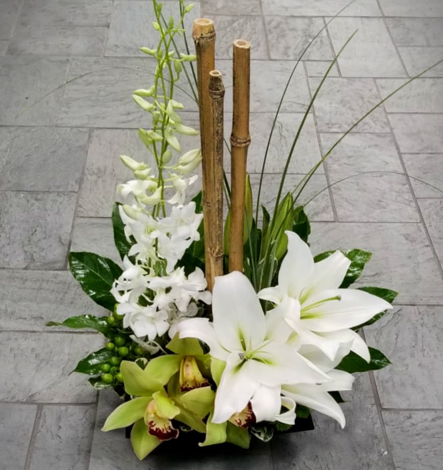 Modern arrangement of white lilies and orchids with bamboo in a low black container