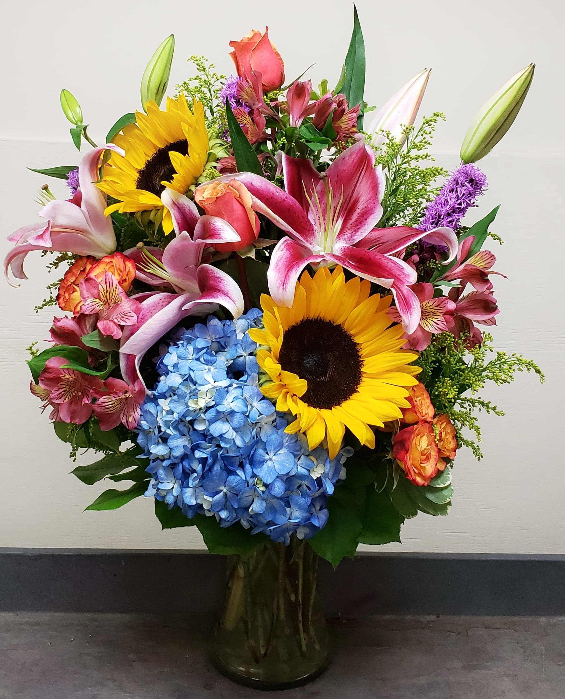 Mixed bouquet with sunflowers, lilies, hydrangeas, and roses in a glass vase