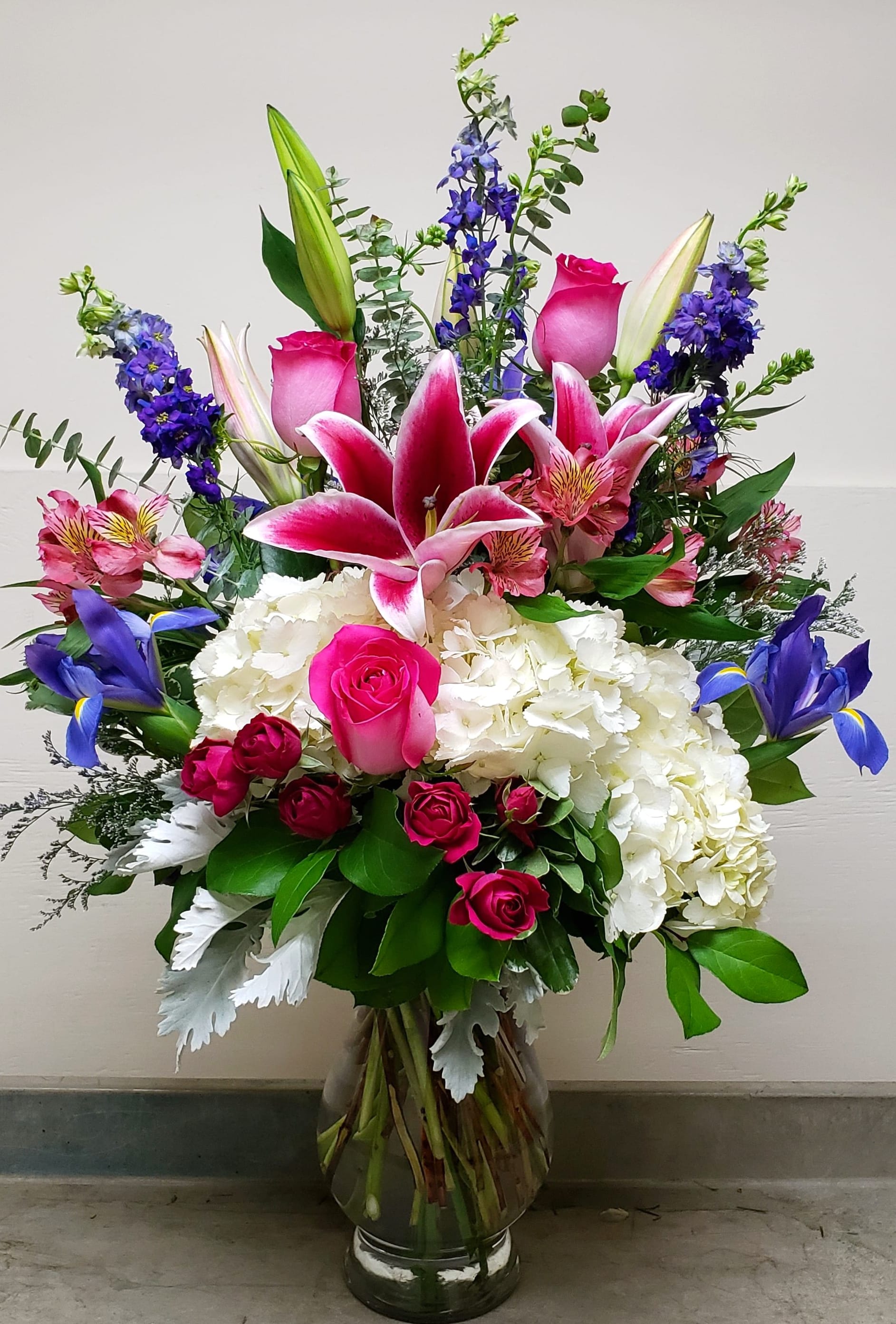 Tall mixed bouquet with pink lilies, roses, hydrangea, and blue iris in a glass vase