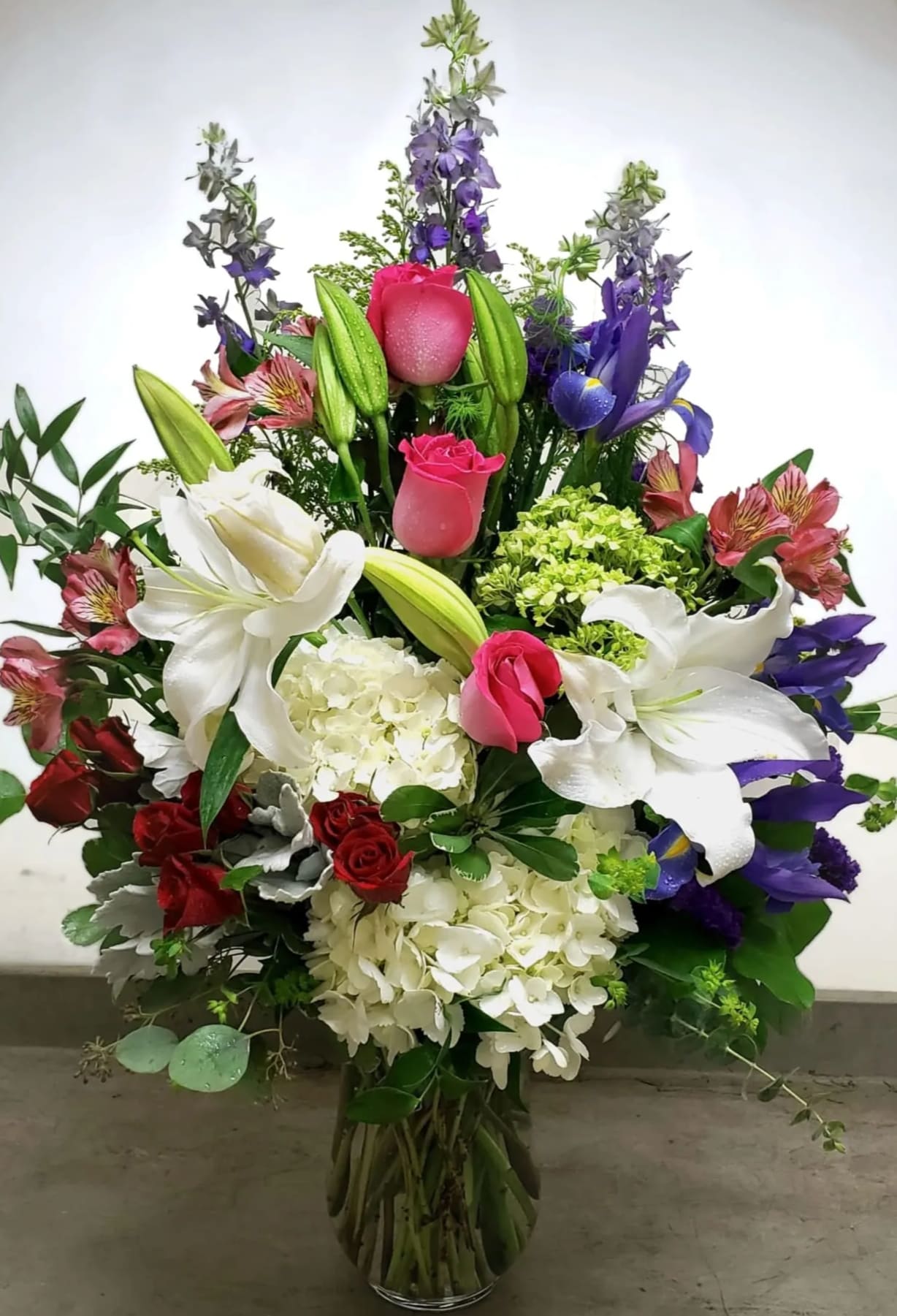 Tall mixed bouquet with white lilies, pink roses, and purple flowers in a glass vase