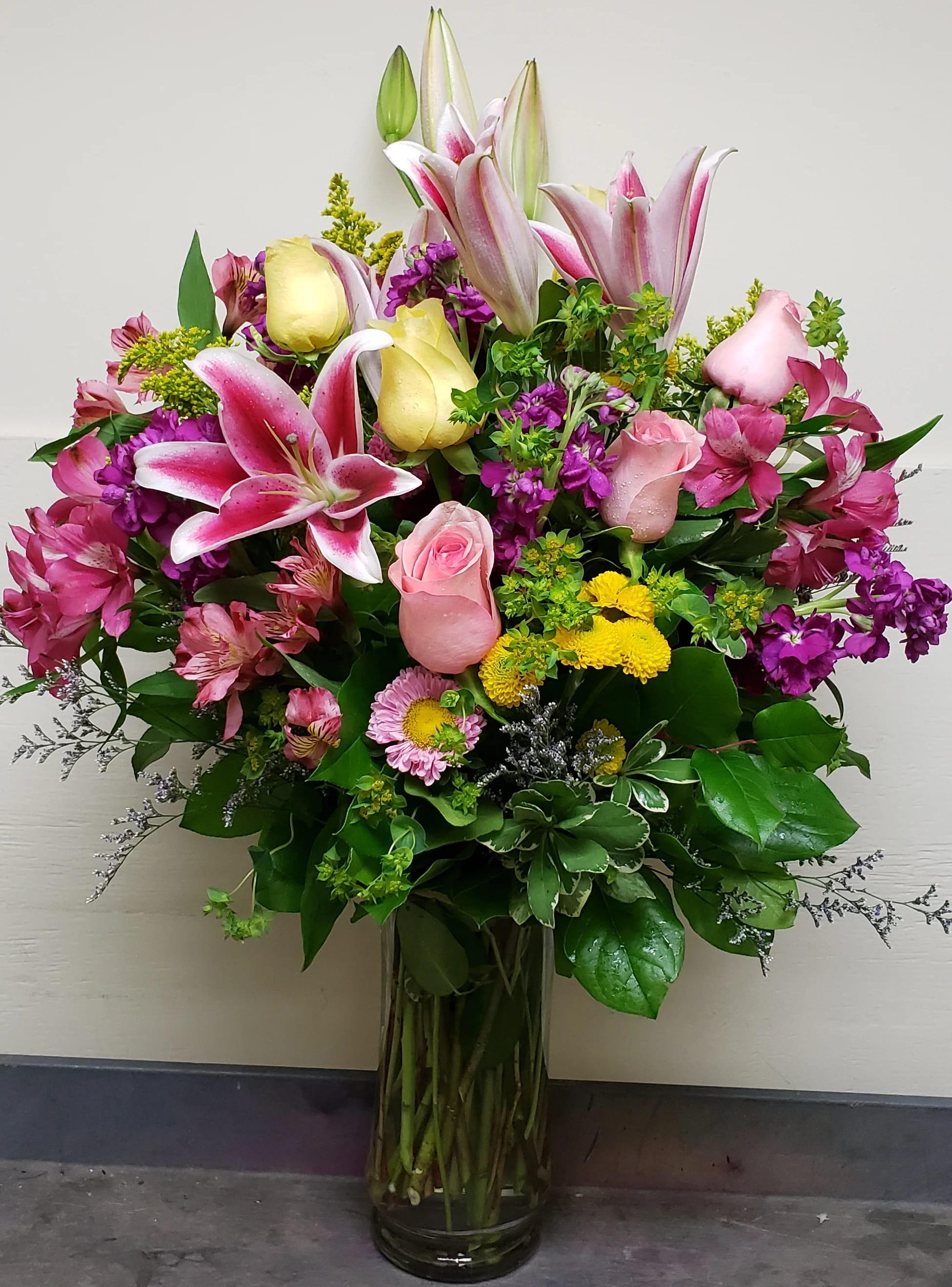 Mixed bouquet of pink lilies, roses, and yellow blooms in a glass vase
