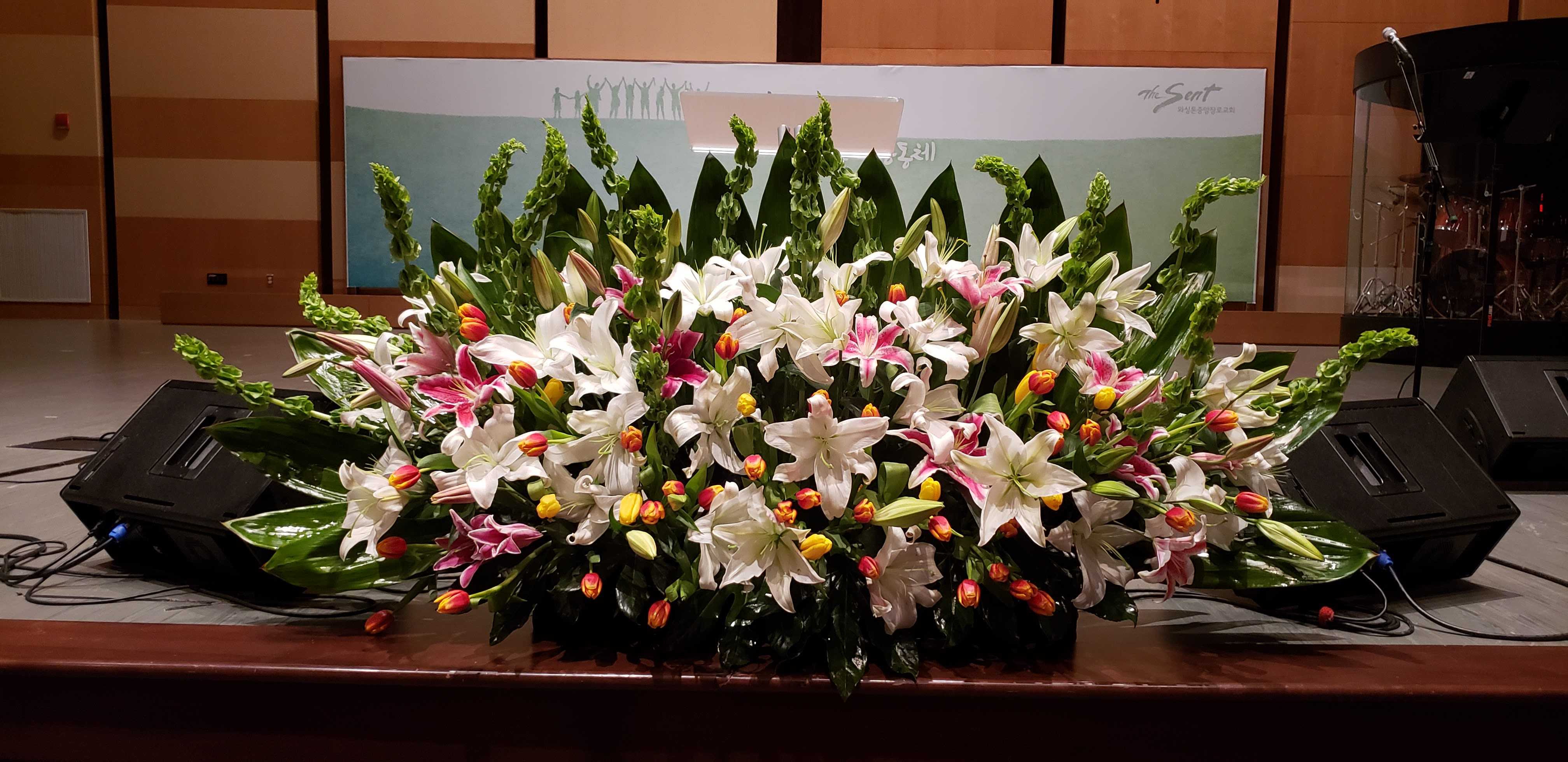 Large stage arrangement of white lilies, pink lilies, and yellow-orange tulips in a wide, low fan shape.