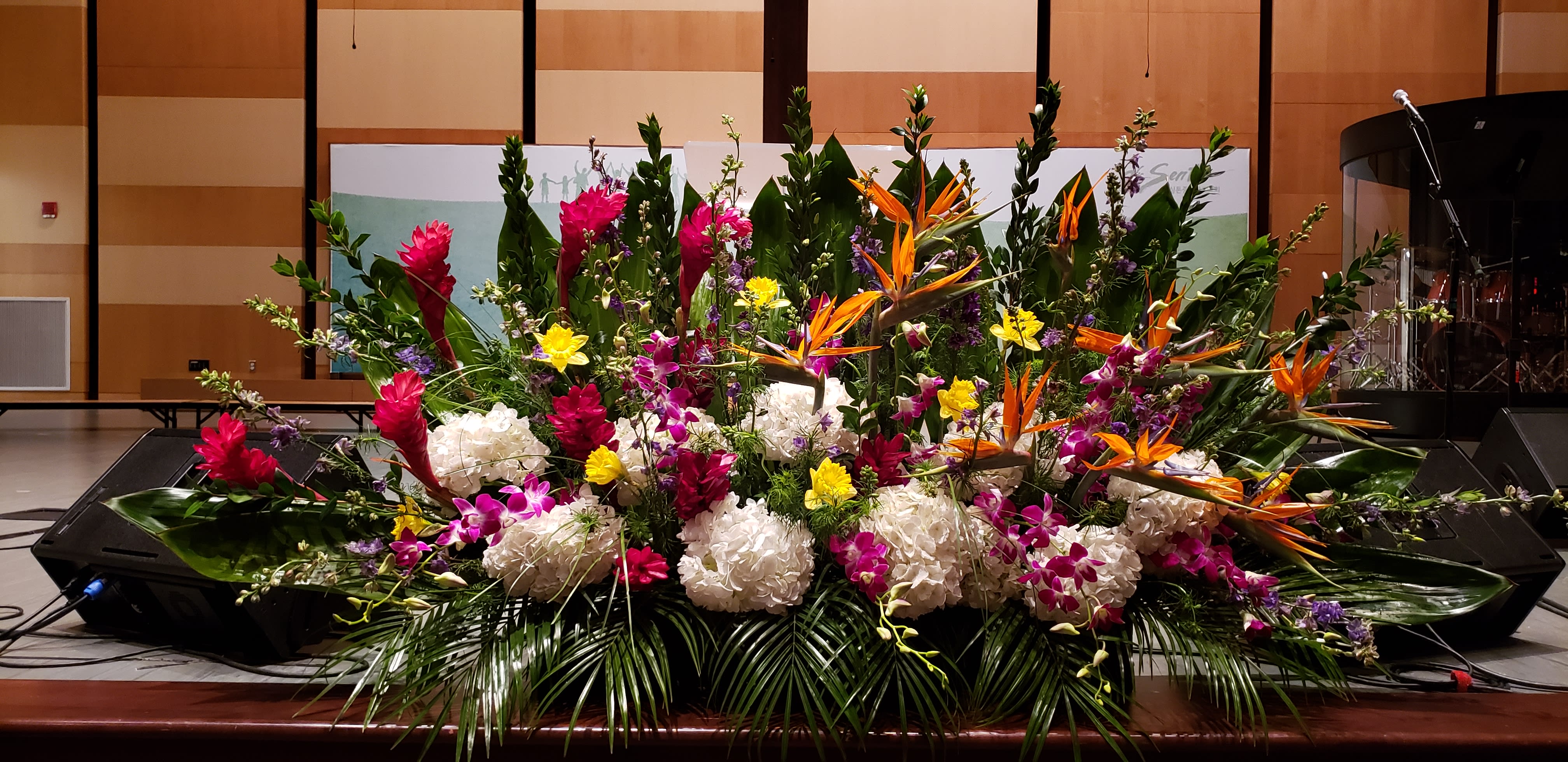 Large tropical stage arrangement with white hydrangeas, orange birds of paradise, and bright accent flowers.