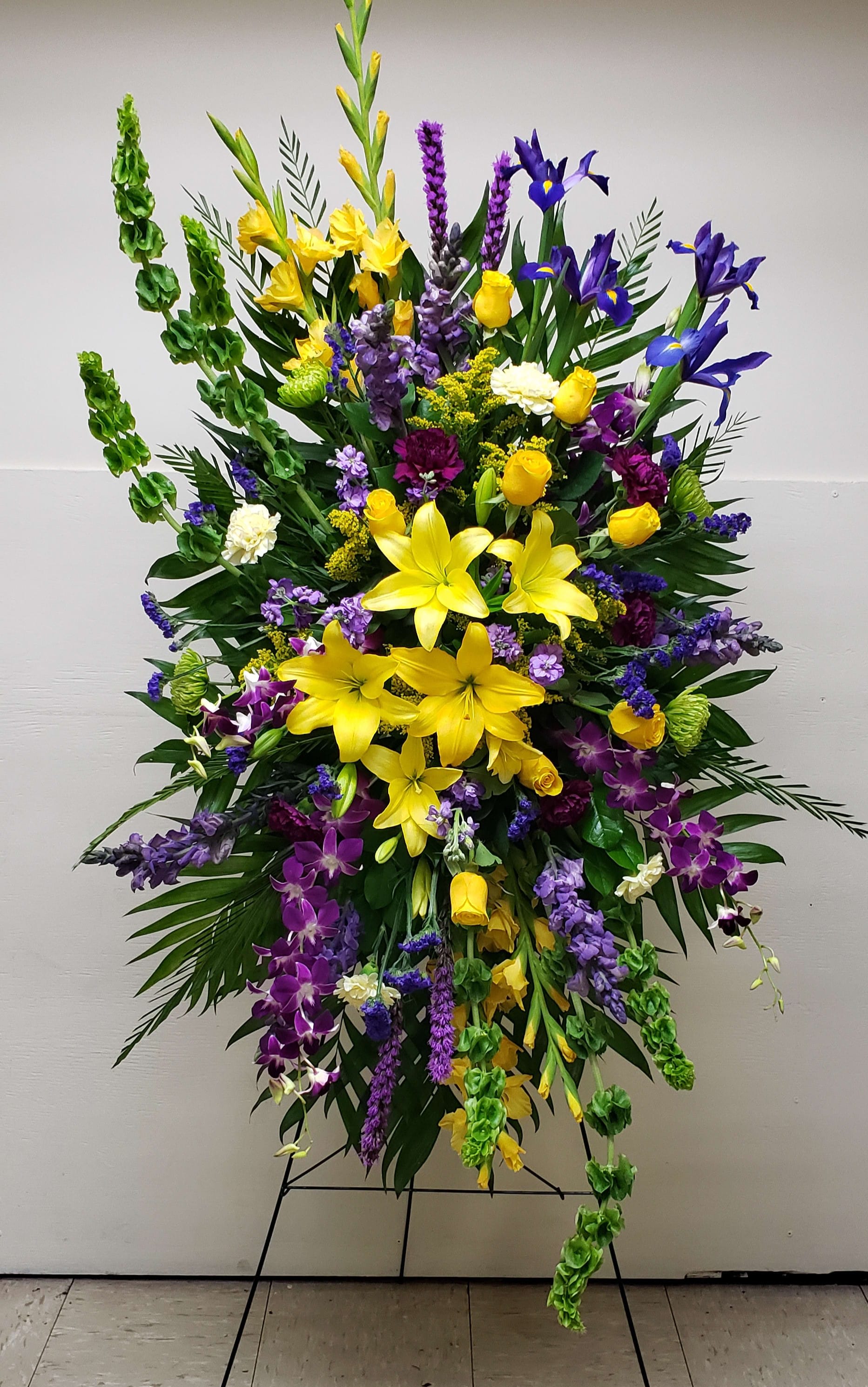 Tall standing spray of yellow lilies, roses, and purple blooms on a metal easel