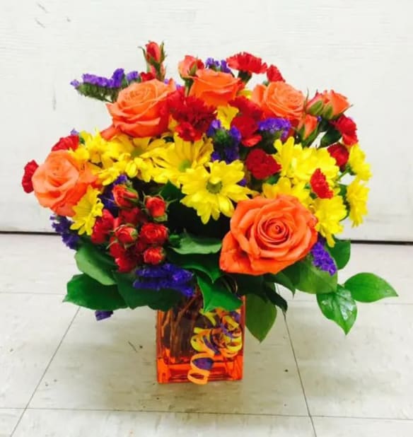 Colorful bouquet of roses and daisies in a square glass vase