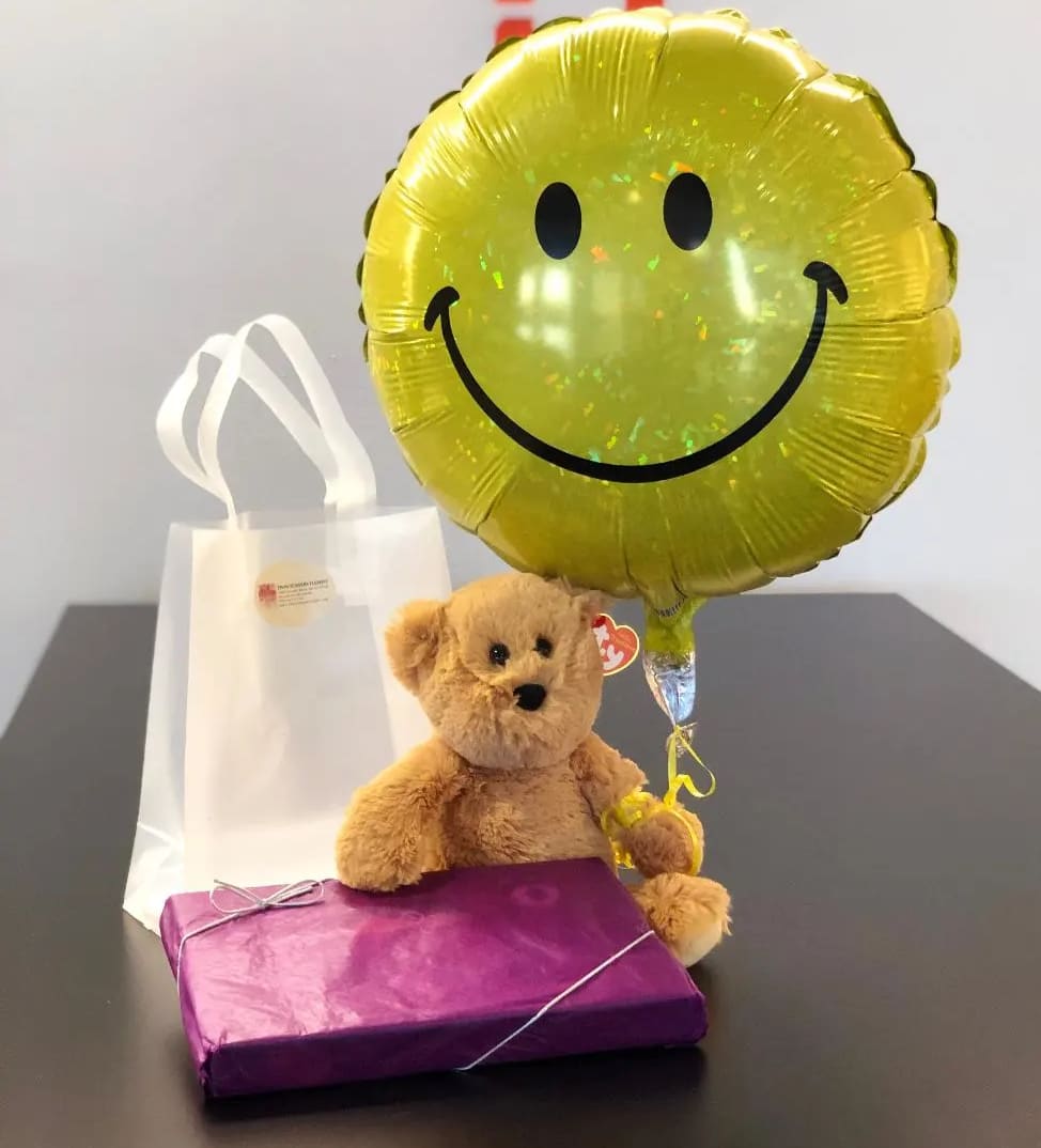 Teddy bear with a smiley balloon, gift bag, and wrapped box