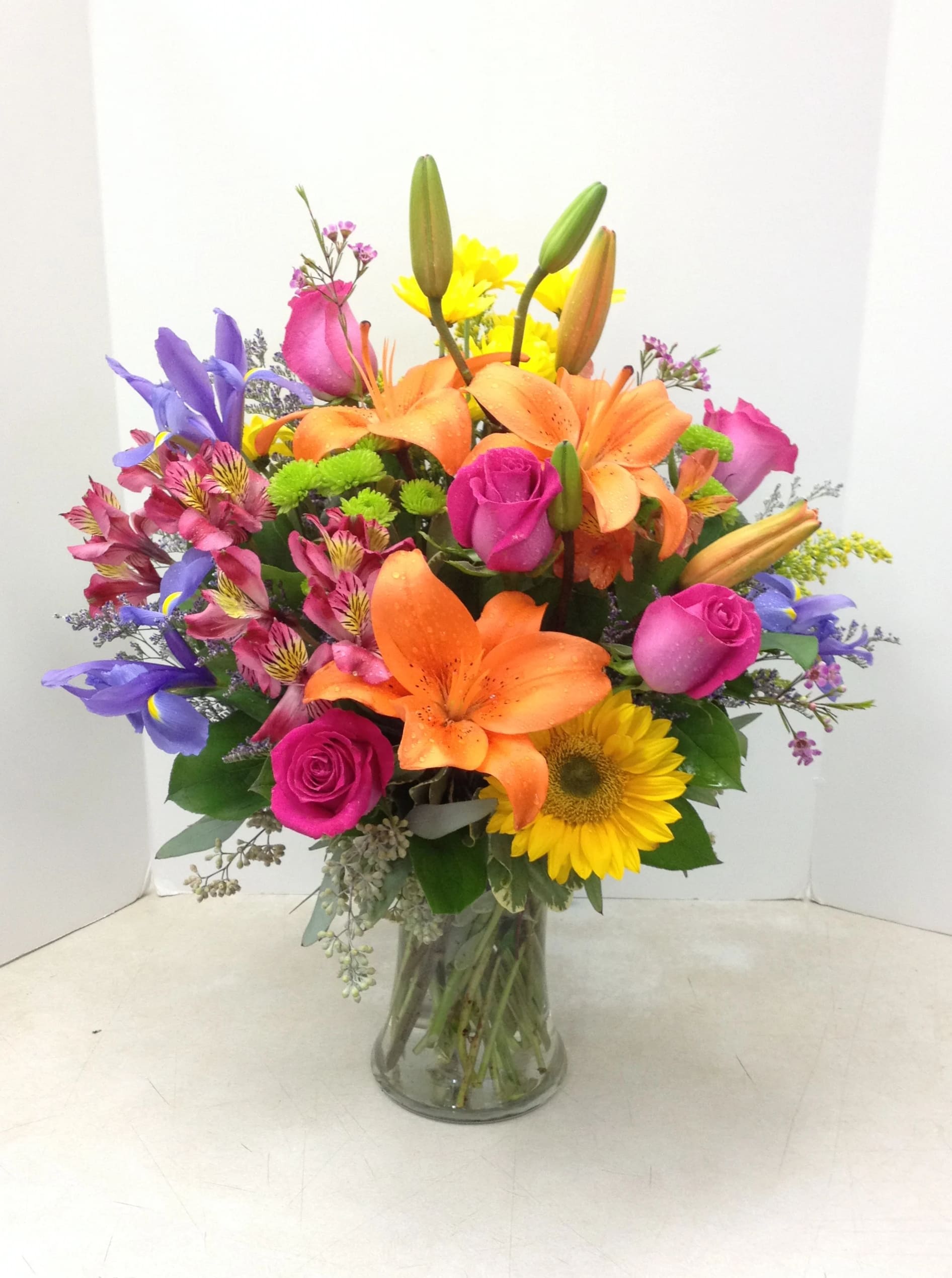 Colorful bouquet of lilies, roses, and a sunflower in a glass vase