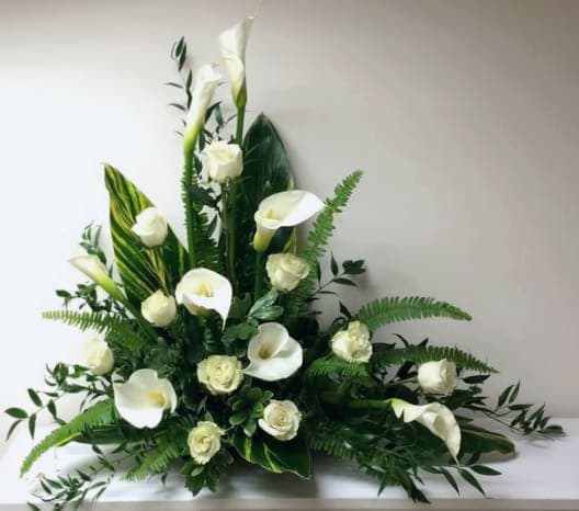 White calla lilies and roses arranged with large glossy leaves in a low, fan-shaped display