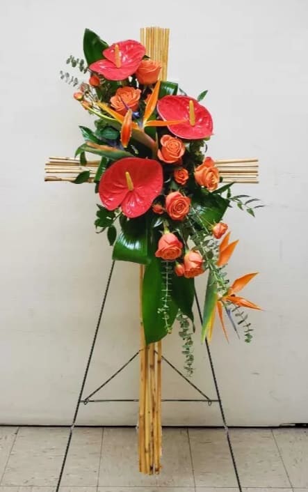 Tall bamboo cross spray with orange roses, red anthuriums, and birds of paradise on a stand