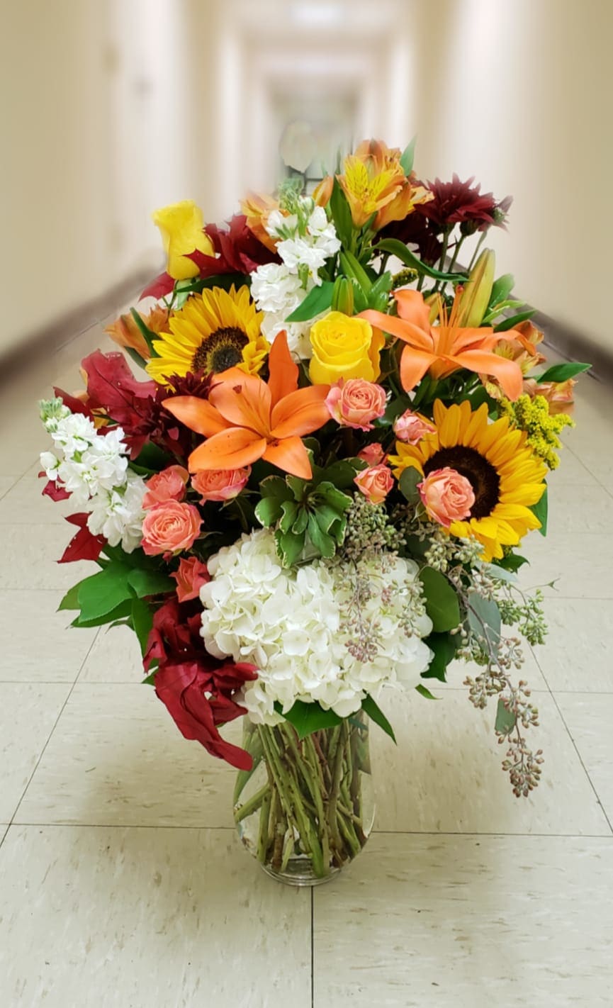 Large mixed bouquet with sunflowers, lilies, roses, and white hydrangeas in a glass vase