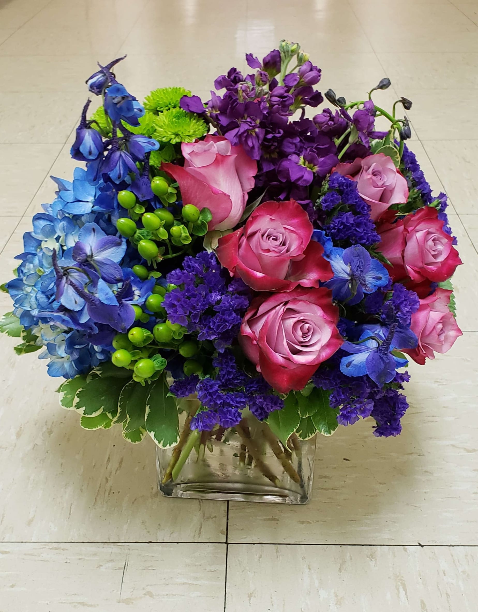 Bouquet of pink roses, blue and purple flowers in a clear glass vase