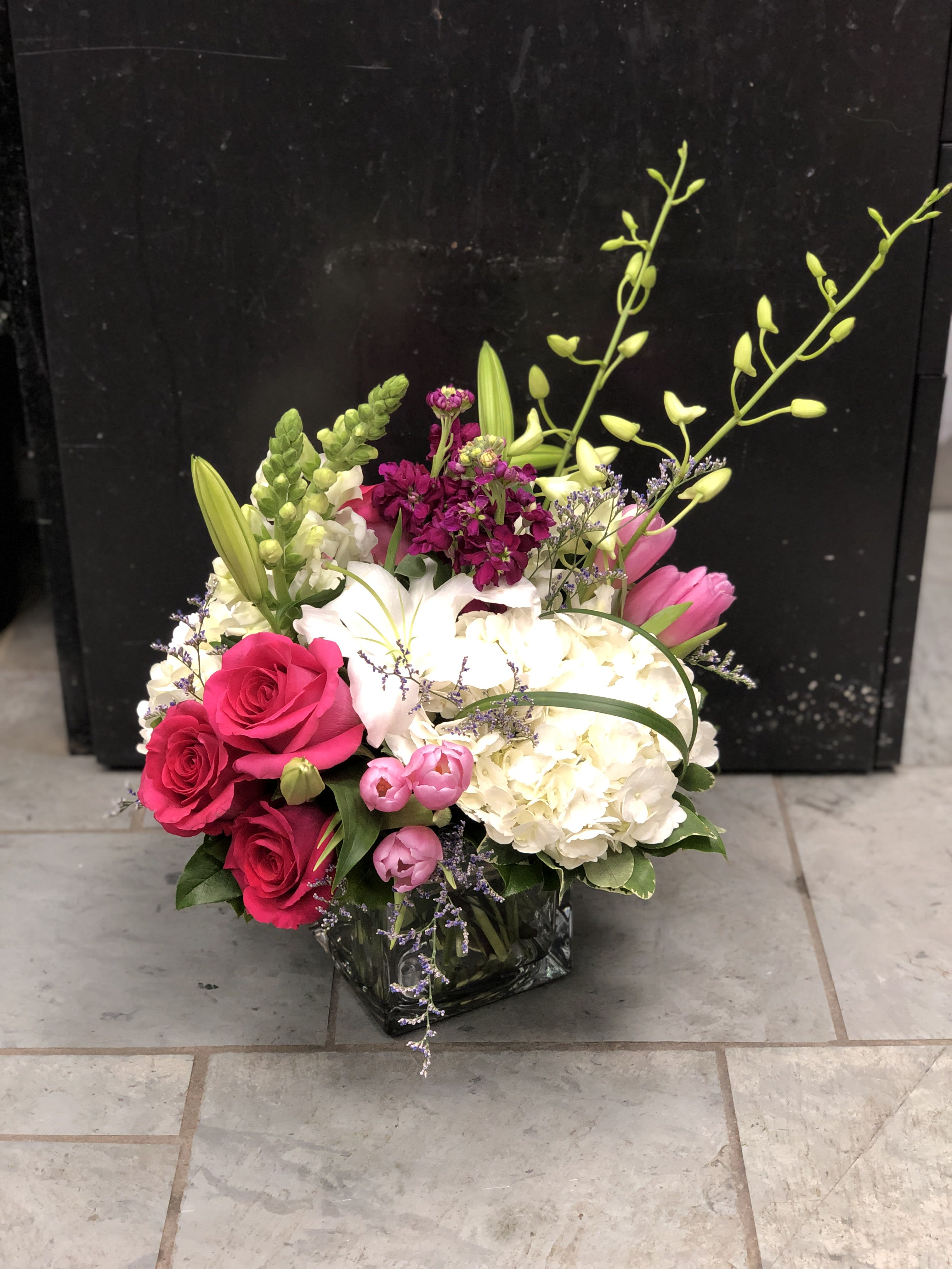 Pink roses and white lilies in a glass vase with hydrangea and orchids