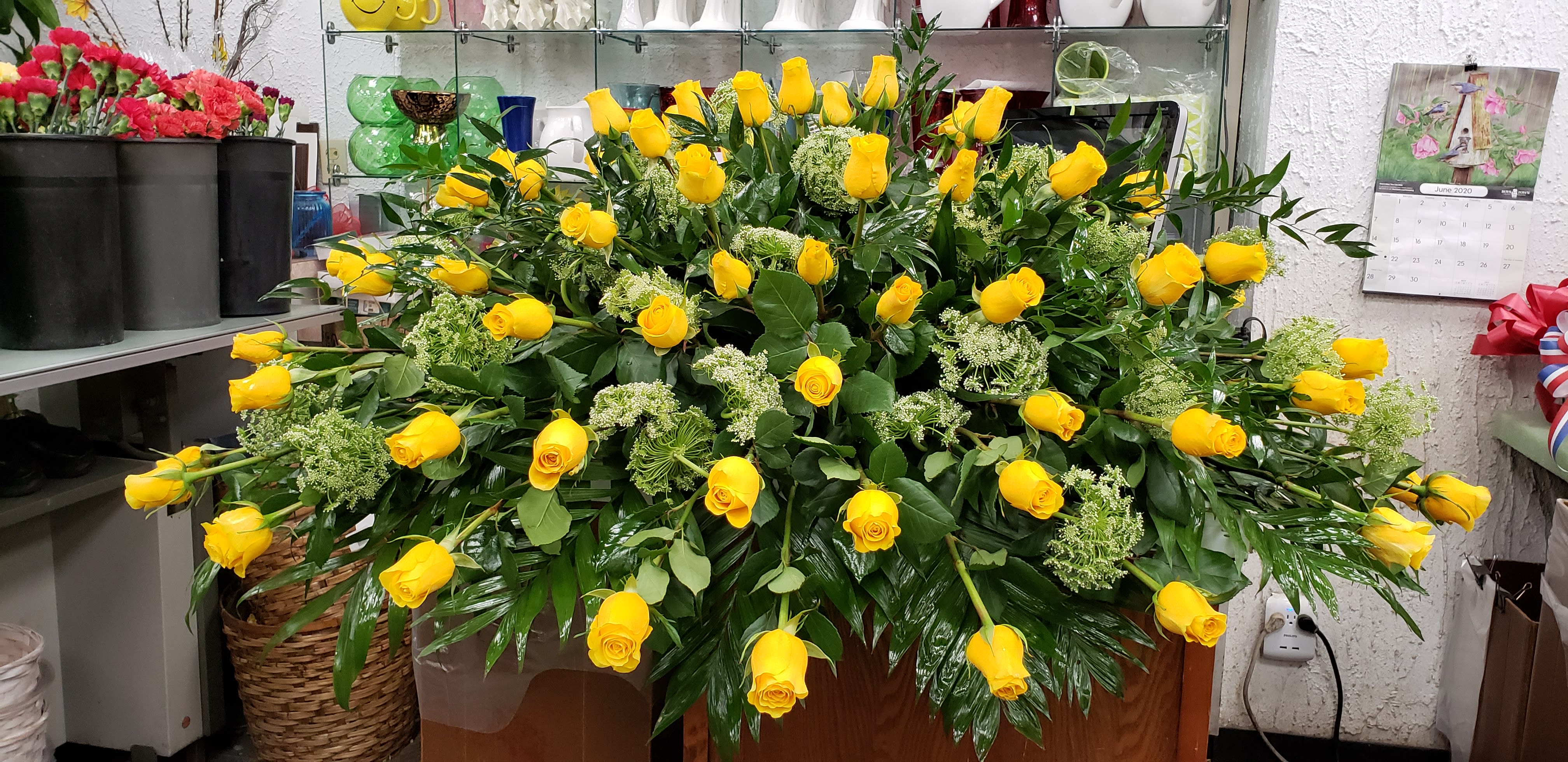 Large horizontal spray of yellow roses with green filler flowers arranged on a wooden base