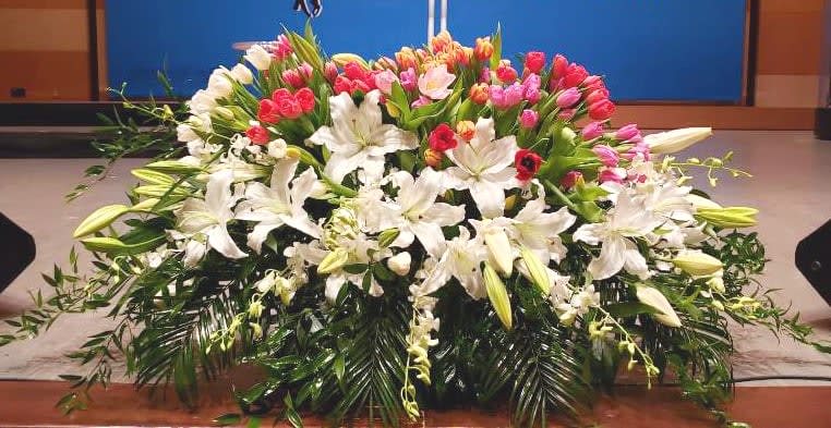 Low spray of white lilies with pink and red tulips arranged in a wide display on a stage.