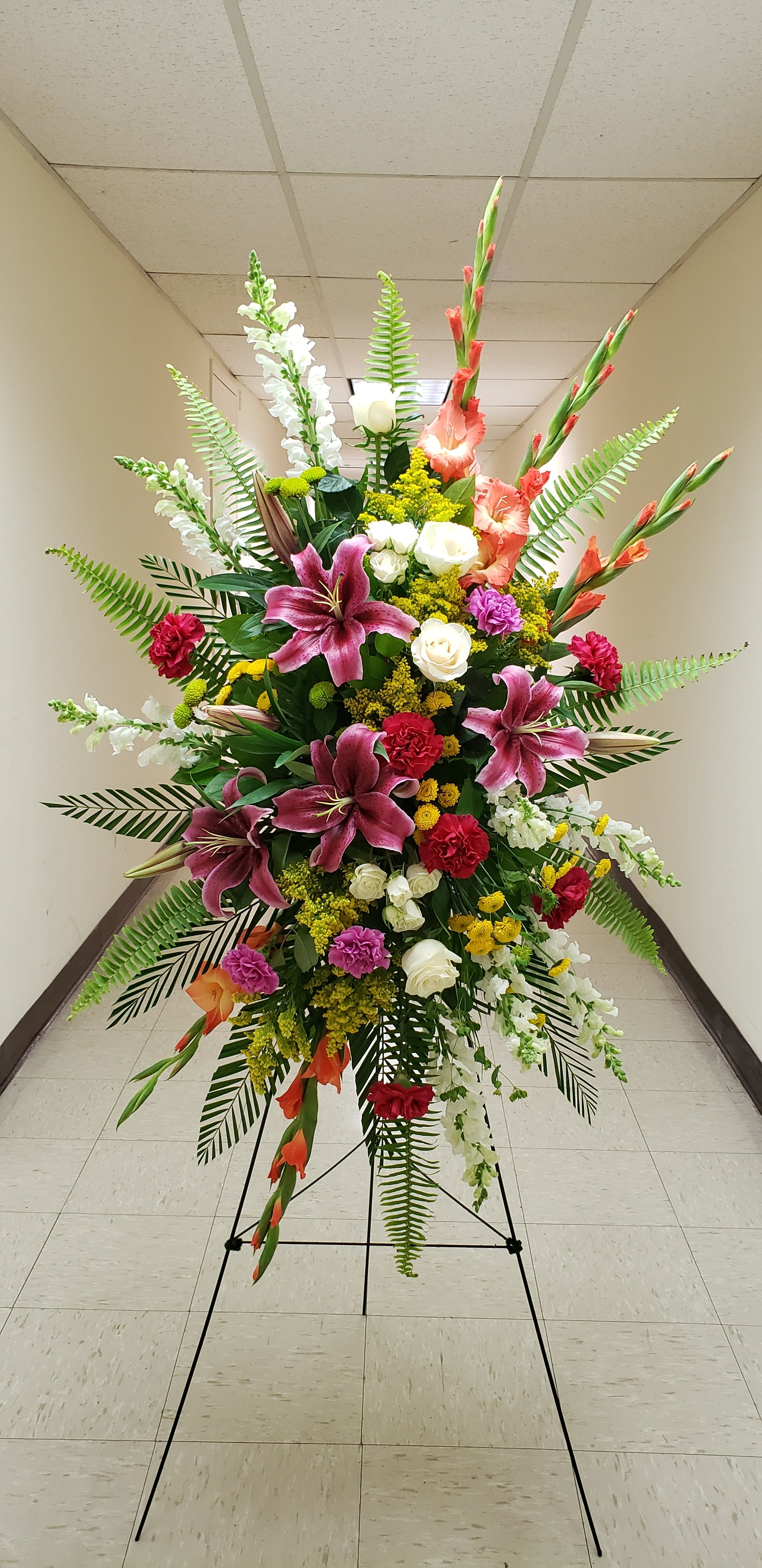 Tall standing spray of pink lilies, red carnations, white roses and mixed flowers on a metal easel