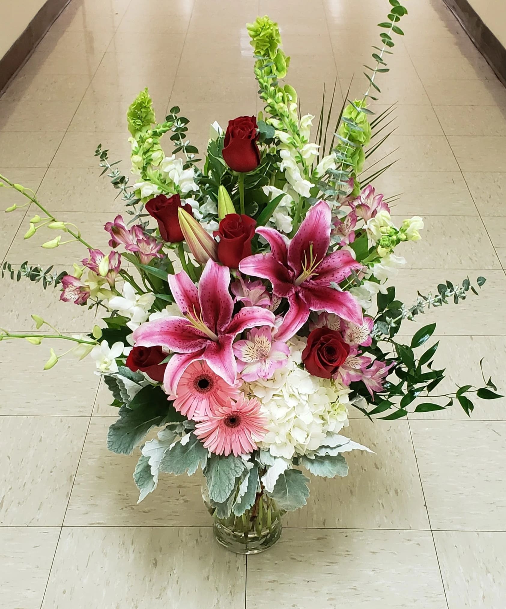 Tall bouquet of pink lilies, red roses, and white blooms in a glass vase