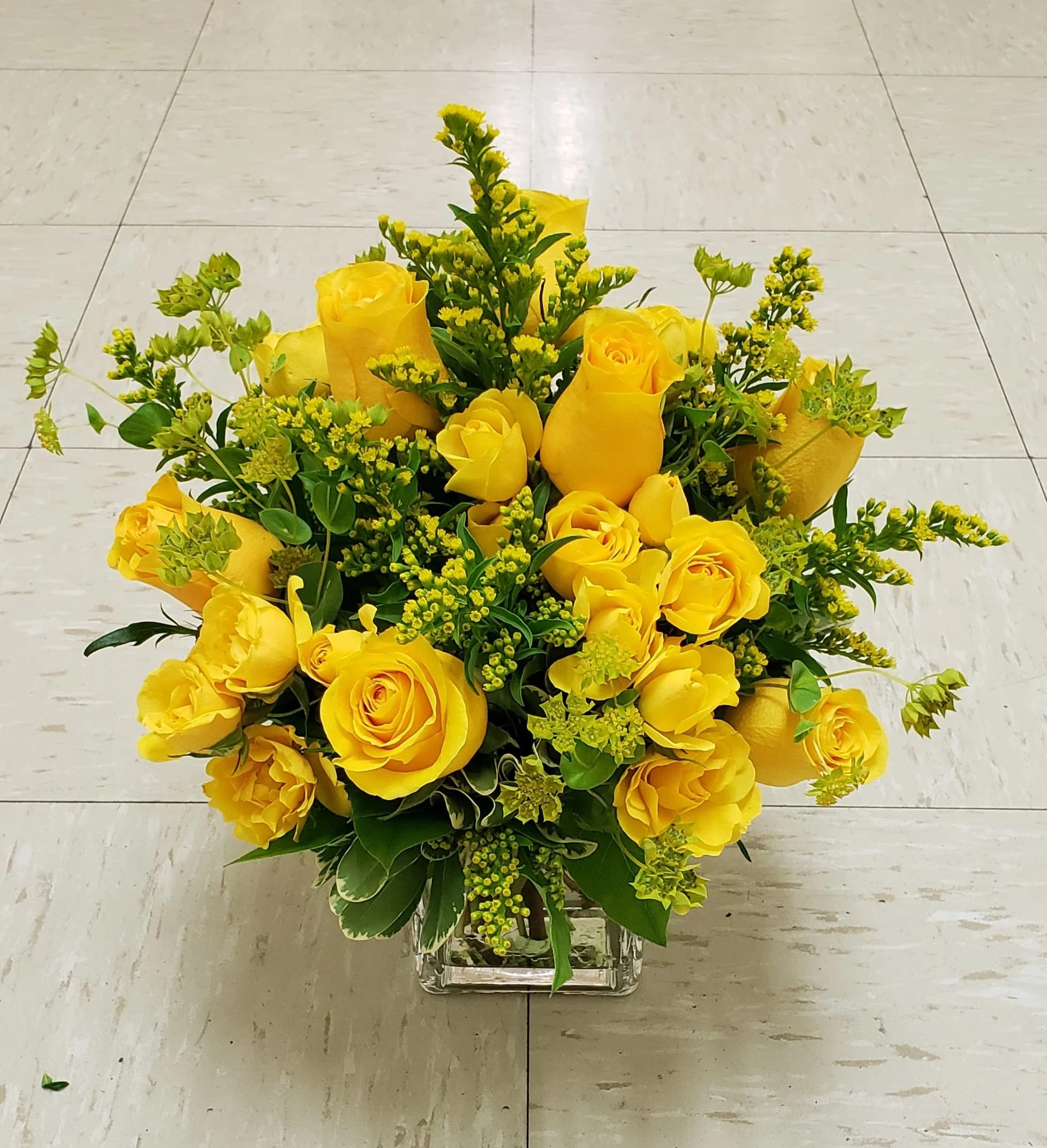 Yellow roses arranged in a clear square vase with green filler flowers